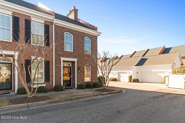 view of property with driveway, a chimney, a gate, fence, and brick siding