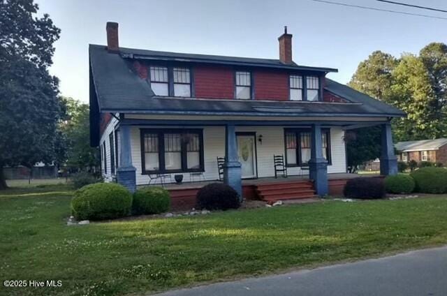 view of front of property with covered porch, a front lawn, and a chimney