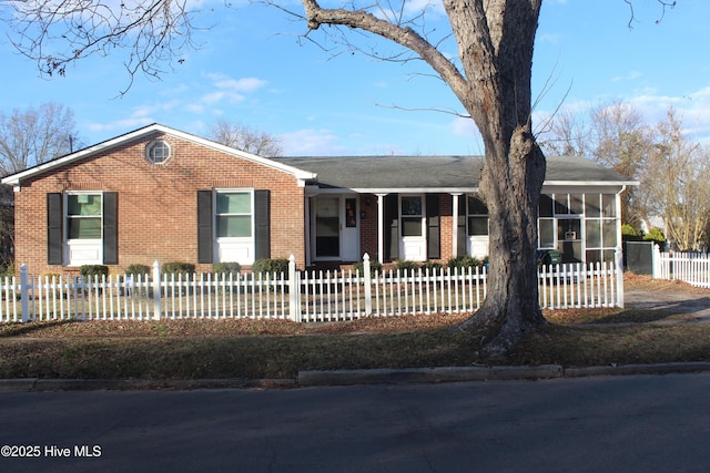 ranch-style home featuring a sunroom, a fenced front yard, and brick siding