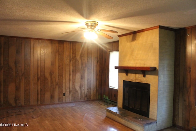 unfurnished living room with a ceiling fan, wood finished floors, baseboard heating, wood walls, and a fireplace