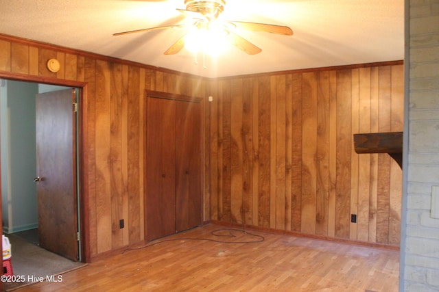 spare room featuring crown molding, wood walls, ceiling fan, and wood finished floors