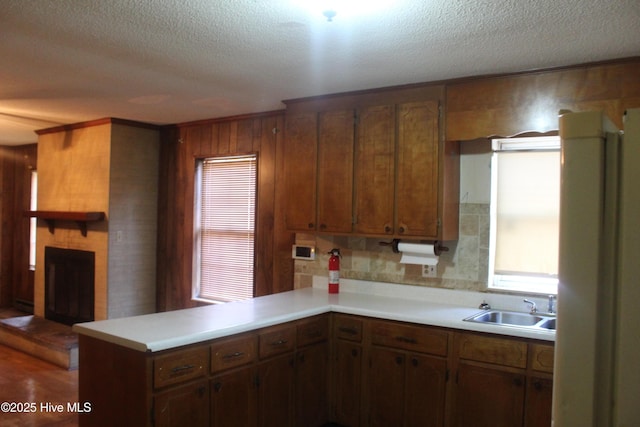 kitchen featuring a fireplace, light countertops, a sink, a textured ceiling, and a peninsula