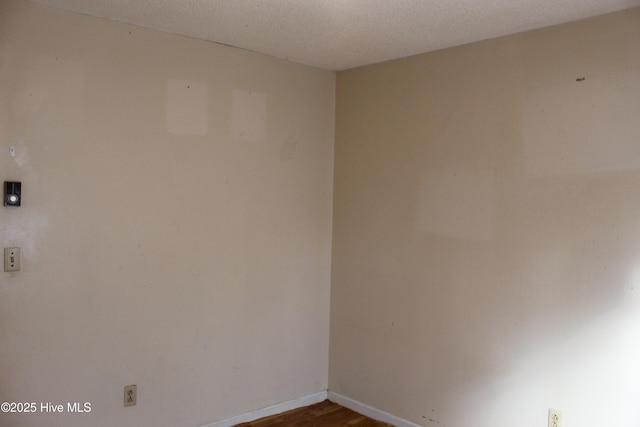 empty room featuring a textured ceiling, dark wood-type flooring, and baseboards