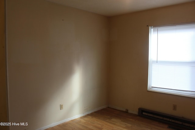 empty room with light wood finished floors, baseboards, and a baseboard heating unit