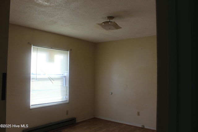 empty room with a textured ceiling, a baseboard radiator, wood finished floors, and baseboards