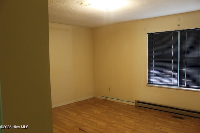 unfurnished room featuring baseboards, visible vents, wood finished floors, a textured ceiling, and a baseboard heating unit