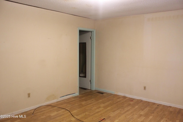 empty room featuring light wood-type flooring, visible vents, a textured ceiling, and baseboards