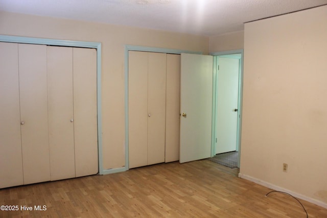 unfurnished bedroom featuring baseboards, two closets, and wood finished floors