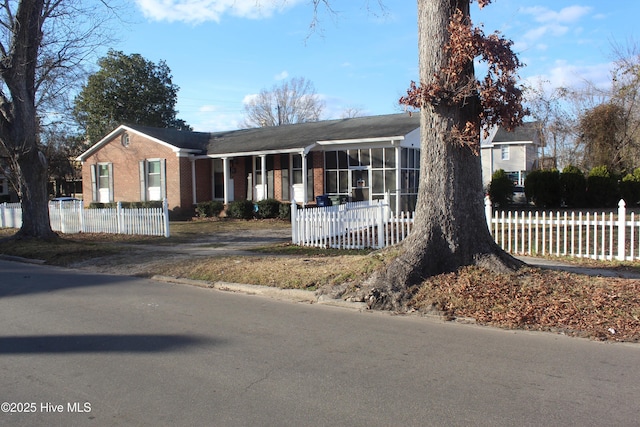 ranch-style house with brick siding, a fenced front yard, and a sunroom