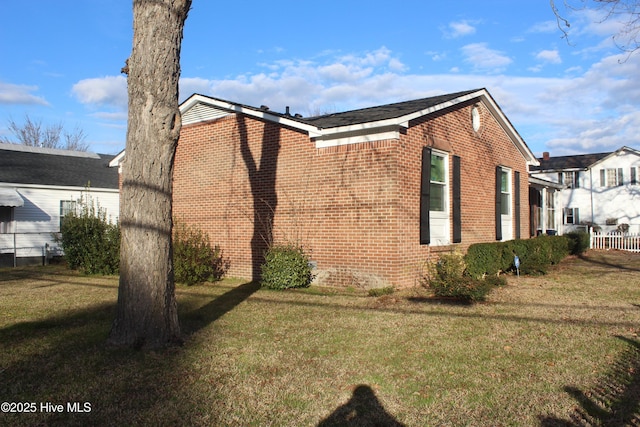 view of property exterior featuring brick siding, a lawn, and fence