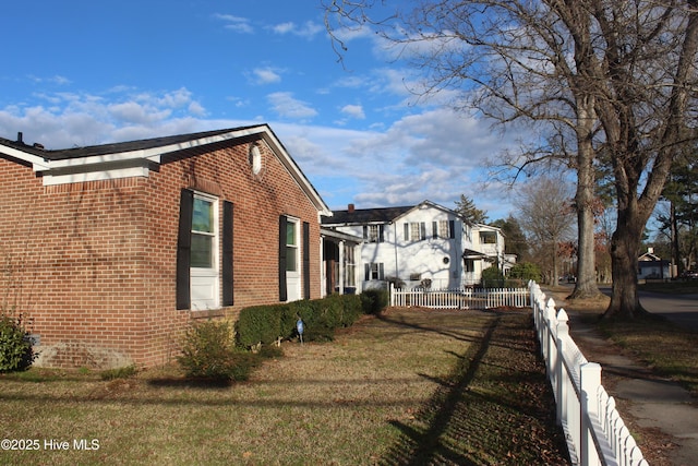 view of side of home with brick siding, a lawn, and fence