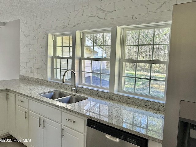 kitchen featuring dishwasher, light stone countertops, a textured ceiling, white cabinetry, and a sink