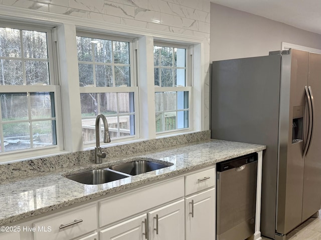 kitchen featuring appliances with stainless steel finishes, a sink, light stone counters, and white cabinets