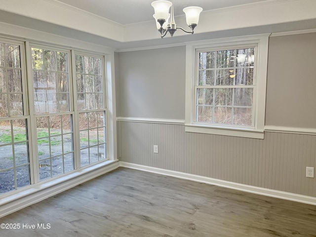 unfurnished dining area with wainscoting, crown molding, an inviting chandelier, and wood finished floors