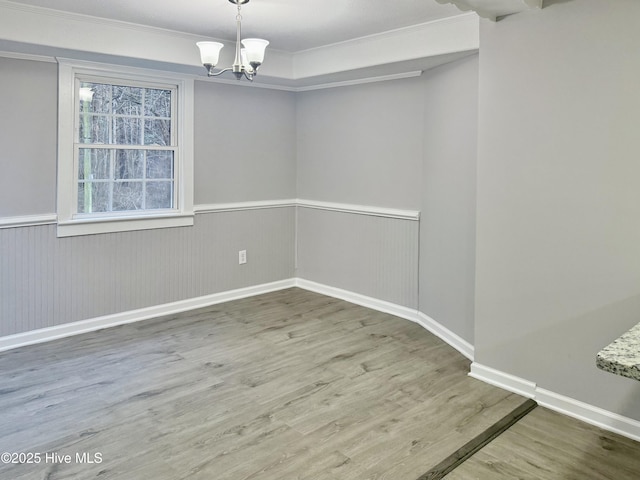 spare room with a notable chandelier, wood finished floors, baseboards, wainscoting, and crown molding