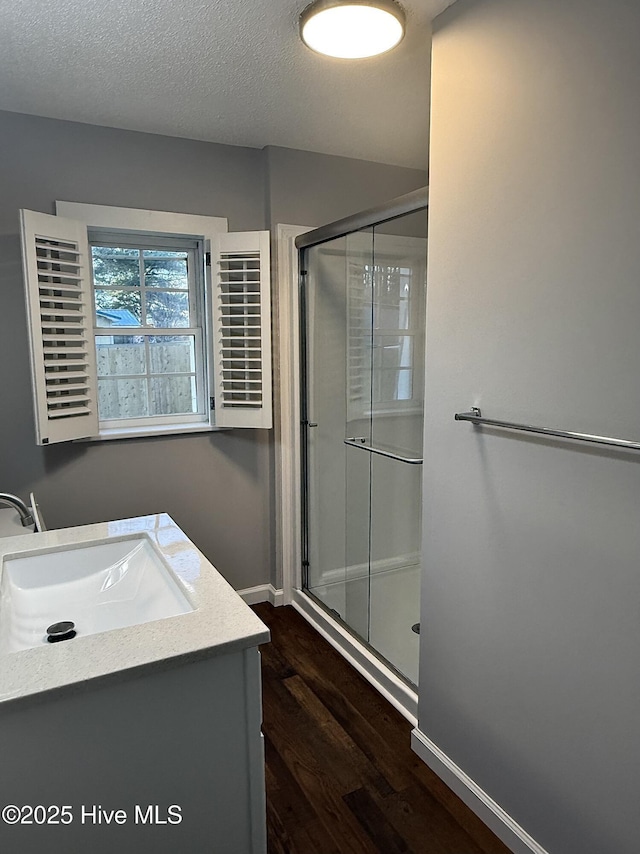 full bathroom featuring baseboards, a shower stall, a textured ceiling, and wood finished floors