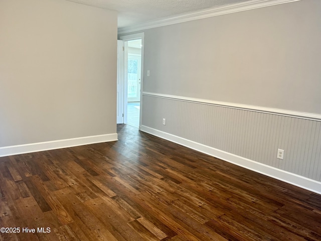 spare room featuring baseboards, a wainscoted wall, dark wood finished floors, and crown molding