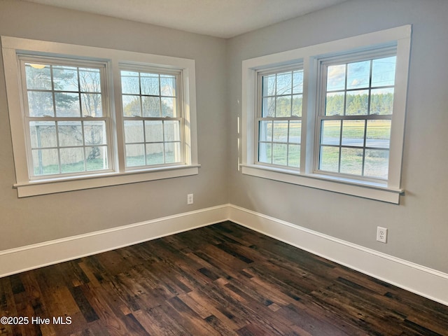 spare room with plenty of natural light, baseboards, and dark wood-style flooring