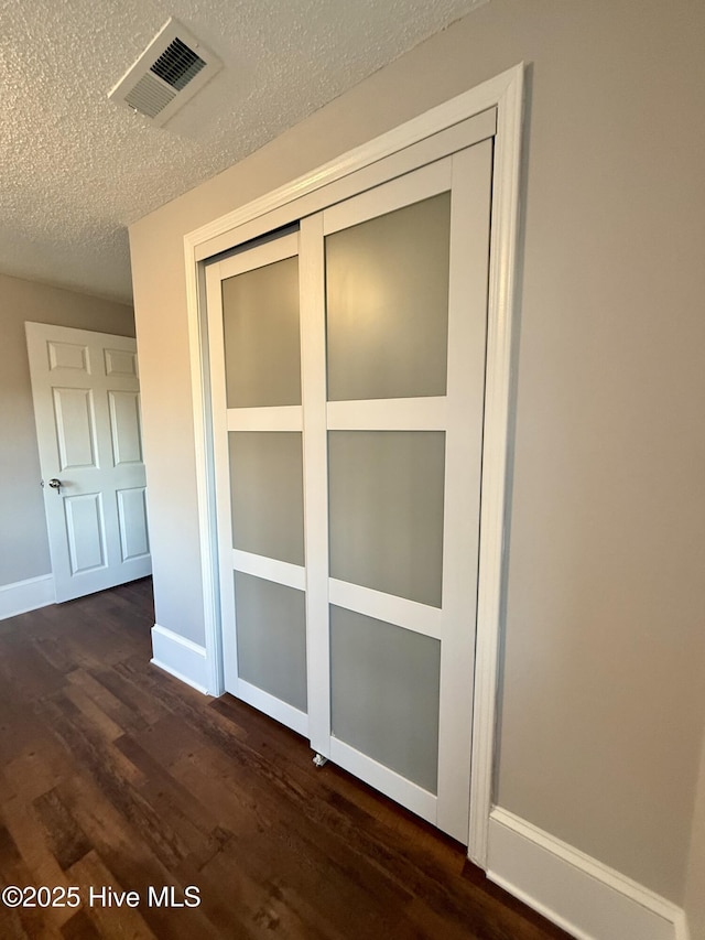 interior space featuring baseboards, a textured ceiling, visible vents, and wood finished floors