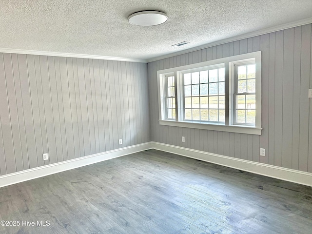 empty room with baseboards, dark wood finished floors, visible vents, and crown molding