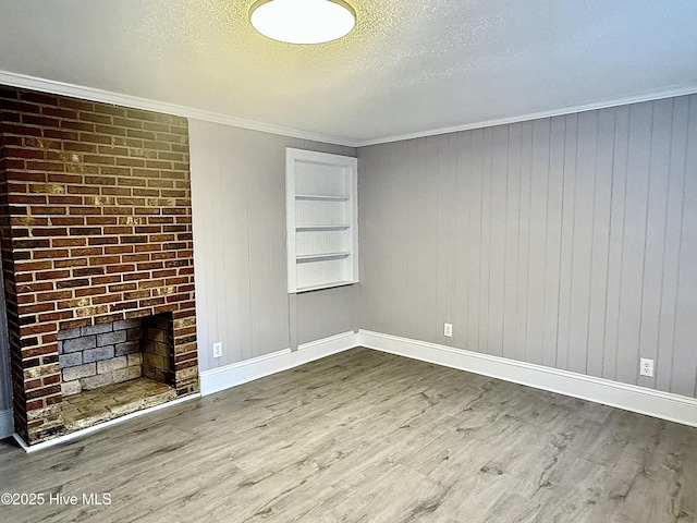 unfurnished room featuring a brick fireplace, crown molding, a textured ceiling, and wood finished floors