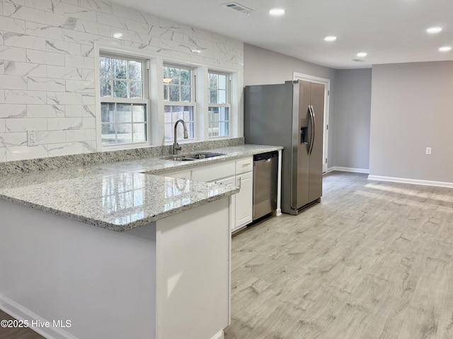 kitchen featuring light stone counters, stainless steel appliances, white cabinets, a sink, and light wood-type flooring