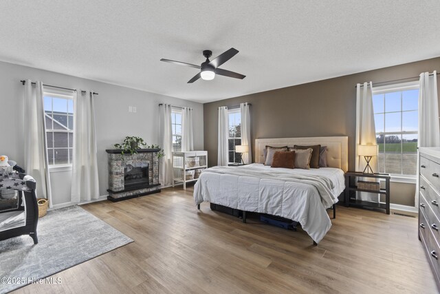 bedroom with light wood finished floors, ceiling fan, a fireplace, and a textured ceiling