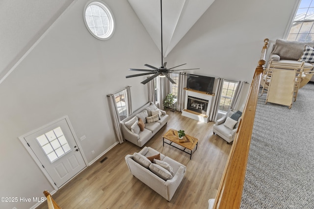 living area with high vaulted ceiling, wood finished floors, visible vents, a ceiling fan, and a glass covered fireplace