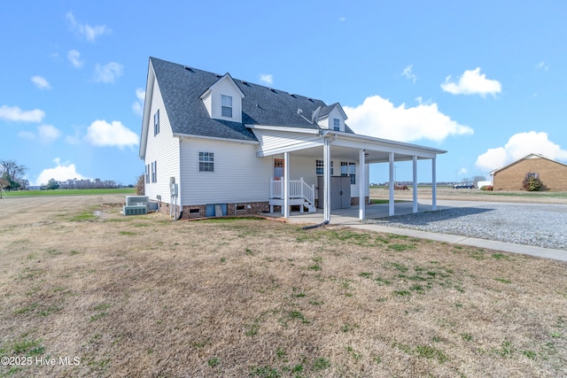 view of front of house with roof with shingles, cooling unit, a carport, and a front yard