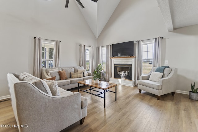 living room featuring a fireplace with raised hearth, high vaulted ceiling, ceiling fan, and light wood-style flooring