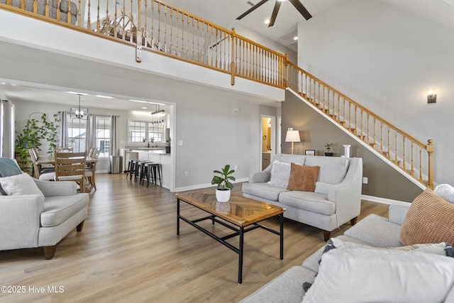 living room featuring stairway, a towering ceiling, wood finished floors, baseboards, and ceiling fan with notable chandelier