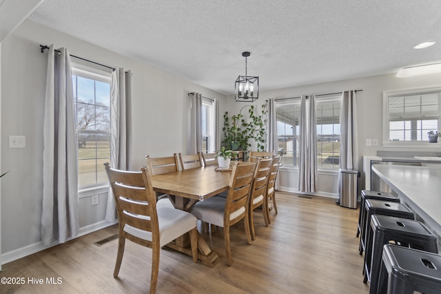 dining space with light wood-style floors, baseboards, a textured ceiling, and an inviting chandelier