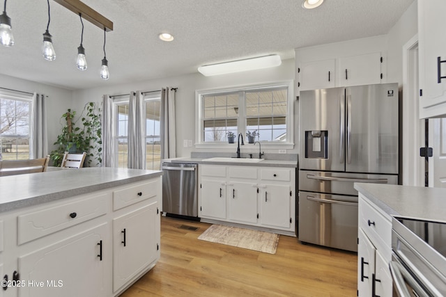 kitchen featuring light countertops, appliances with stainless steel finishes, white cabinets, a sink, and light wood-type flooring