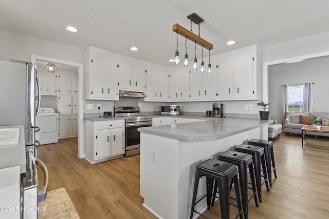 kitchen with under cabinet range hood, light countertops, appliances with stainless steel finishes, light wood finished floors, and washer / dryer