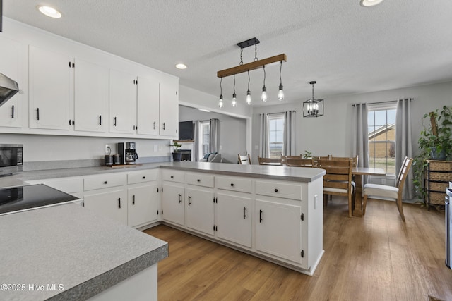 kitchen featuring a peninsula, light wood finished floors, cooktop, and white cabinets