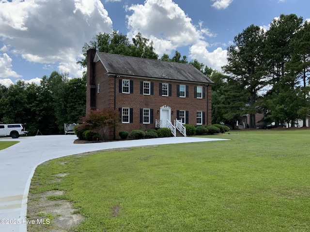 colonial house featuring brick siding, a chimney, and a front yard