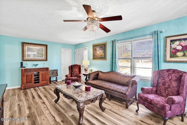 living area with baseboards, a textured ceiling, light wood-style flooring, and a ceiling fan