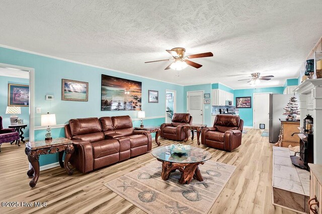 living room featuring a ceiling fan, baseboards, a textured ceiling, crown molding, and light wood-type flooring