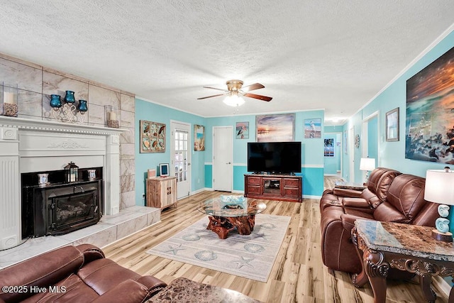 living area featuring a textured ceiling, a fireplace with raised hearth, wood finished floors, and ornamental molding