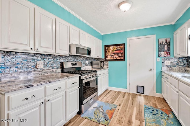 kitchen featuring light wood-type flooring, appliances with stainless steel finishes, ornamental molding, and white cabinetry