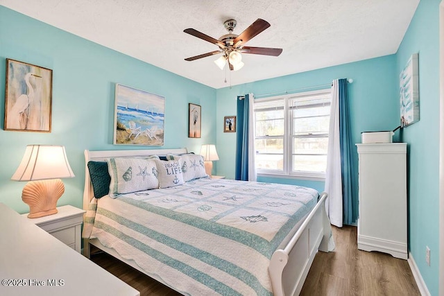 bedroom featuring ceiling fan, baseboards, a textured ceiling, and wood finished floors