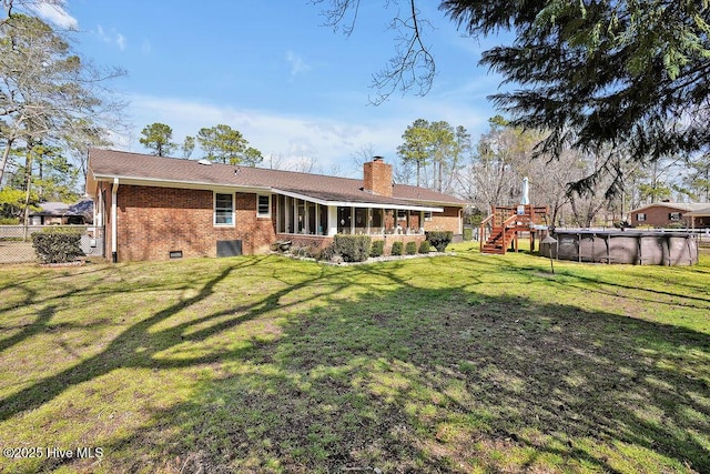 rear view of house with an outdoor pool, a sunroom, a chimney, a lawn, and brick siding