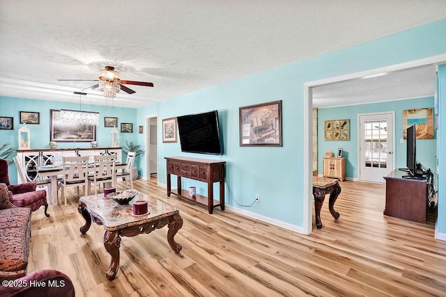 living room with ceiling fan, light wood-style flooring, baseboards, and a textured ceiling