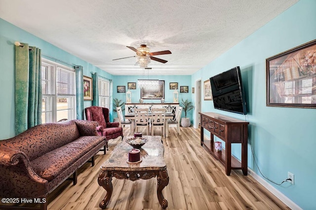 living area featuring light wood finished floors, baseboards, a textured ceiling, and a ceiling fan