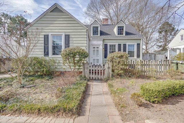 cape cod house with a fenced front yard, a shingled roof, and a chimney