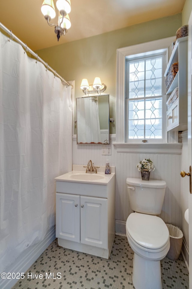 full bathroom featuring a wainscoted wall, toilet, an inviting chandelier, vanity, and a shower with curtain