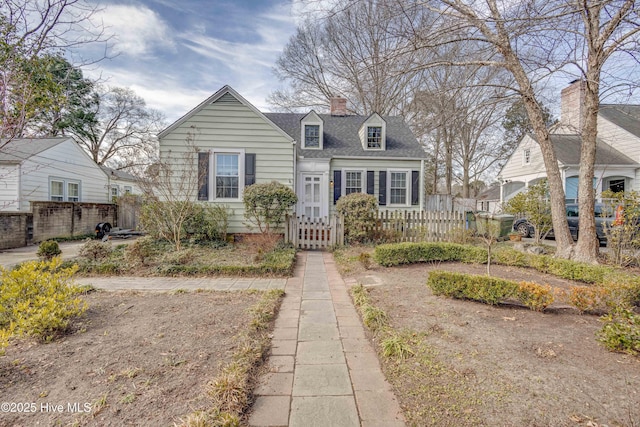 new england style home with roof with shingles, a fenced front yard, and a chimney