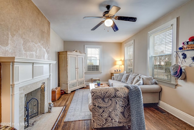 living area featuring a fireplace with raised hearth, visible vents, ceiling fan, wood finished floors, and baseboards