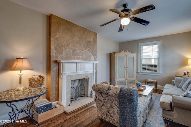 living area featuring a ceiling fan, baseboards, a fireplace with raised hearth, and wood finished floors