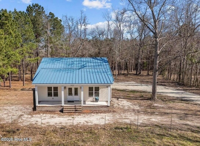 view of outbuilding with covered porch, a wooded view, and french doors